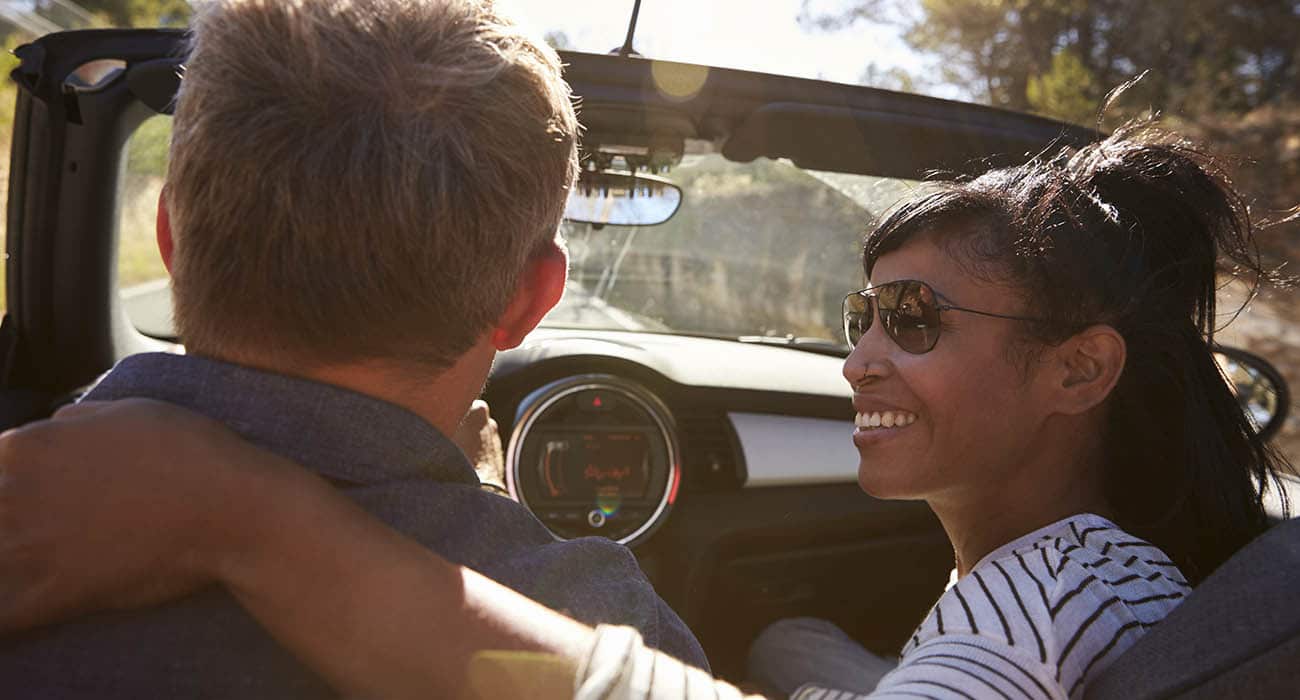 Two people sitting together at a table, smiling and looking at a smartphone that one of them is holding, in a brightly lit indoor setting.