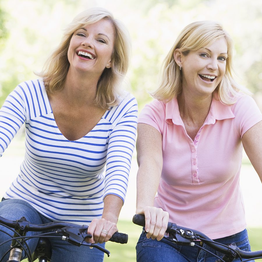 Two chefs wearing white uniforms smile and talk together in a professional kitchen, with industrial vents visible in the background.