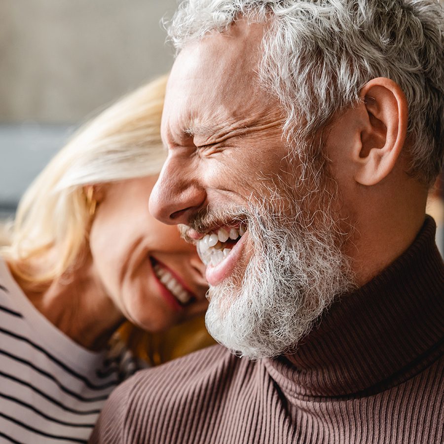 Silhouettes of a man and two children playing joyfully on the beach at sunset, with the sun low in the sky and waves in the background.
